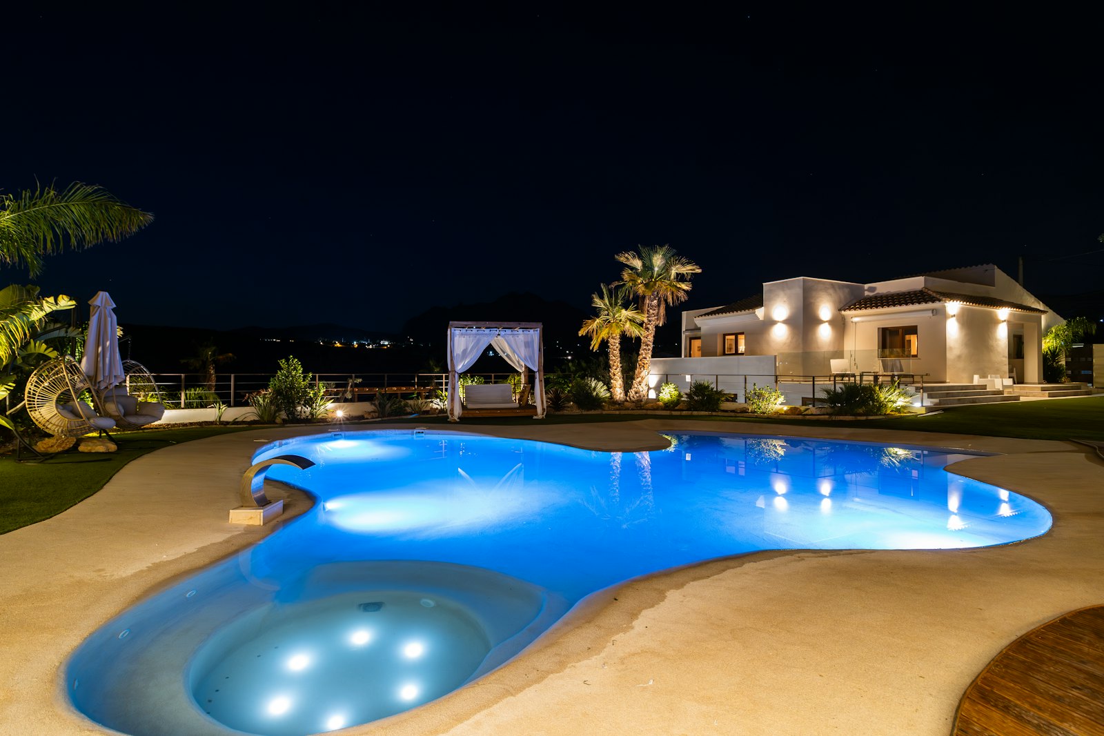 A lit villa and pool at night, palms against a dark sky